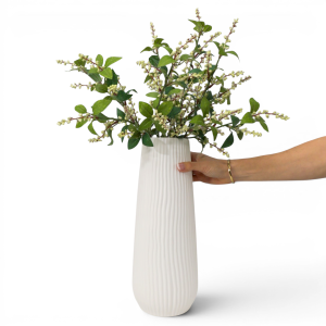 Hand holding the Tall Zahra Ribbed White Vase with green foliage and pale buds to show its scale